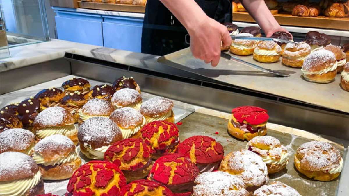 Entdecken Sie die lustige Tradition, wie Kinder Eltern mit einem dekorierten Holzstab wecken, um nach den leckeren Brötchen zu verlangen, und genießen Sie die süße Köstlichkeit mit Marmelade, Sahne und Schokoladenglasur.